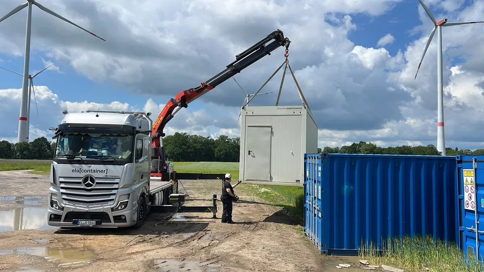 Kran-LKW hebt einen Container vor Windrädern im Emsland