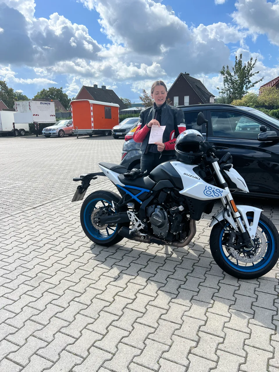 Fahrschülerin mit ihrer bestandenen Prüfungsbescheinigung neben einem Motorrad
