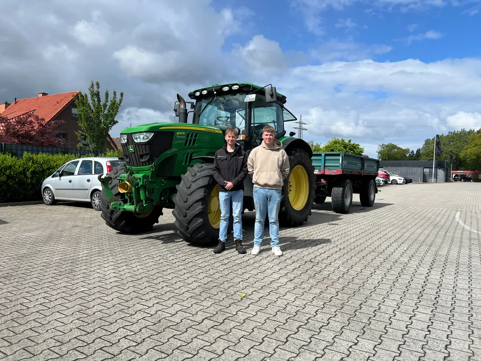 Zwei Fahrschüler vor einem John-Deere-Traktor mit Anhänger der Fahrschule Rüther
