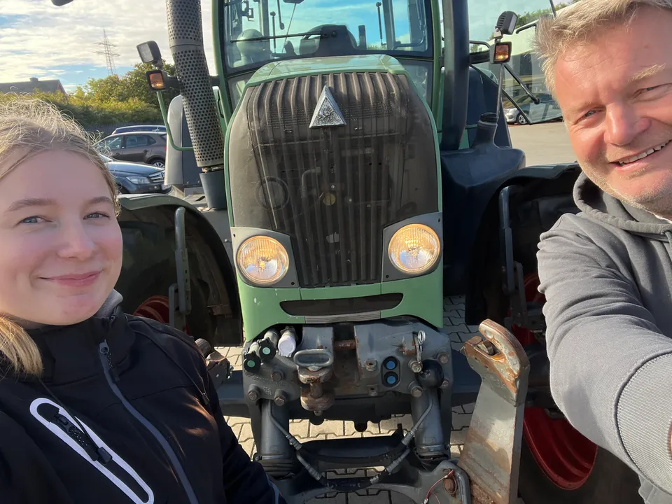 Fahrlehrer und Fahrschülerin lächeln vor einem Traktor der Fahrschule Rüther